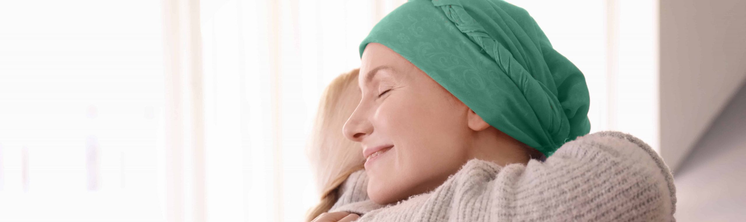 Woman with cancer and green bandanna hugging friend